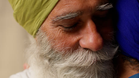 Close-Up-Studio-Shot-Of-Senior-Sikh-Father-Embracing-Adult-Son-Both-Wearing-Turbans-Against-Plain-Background-1